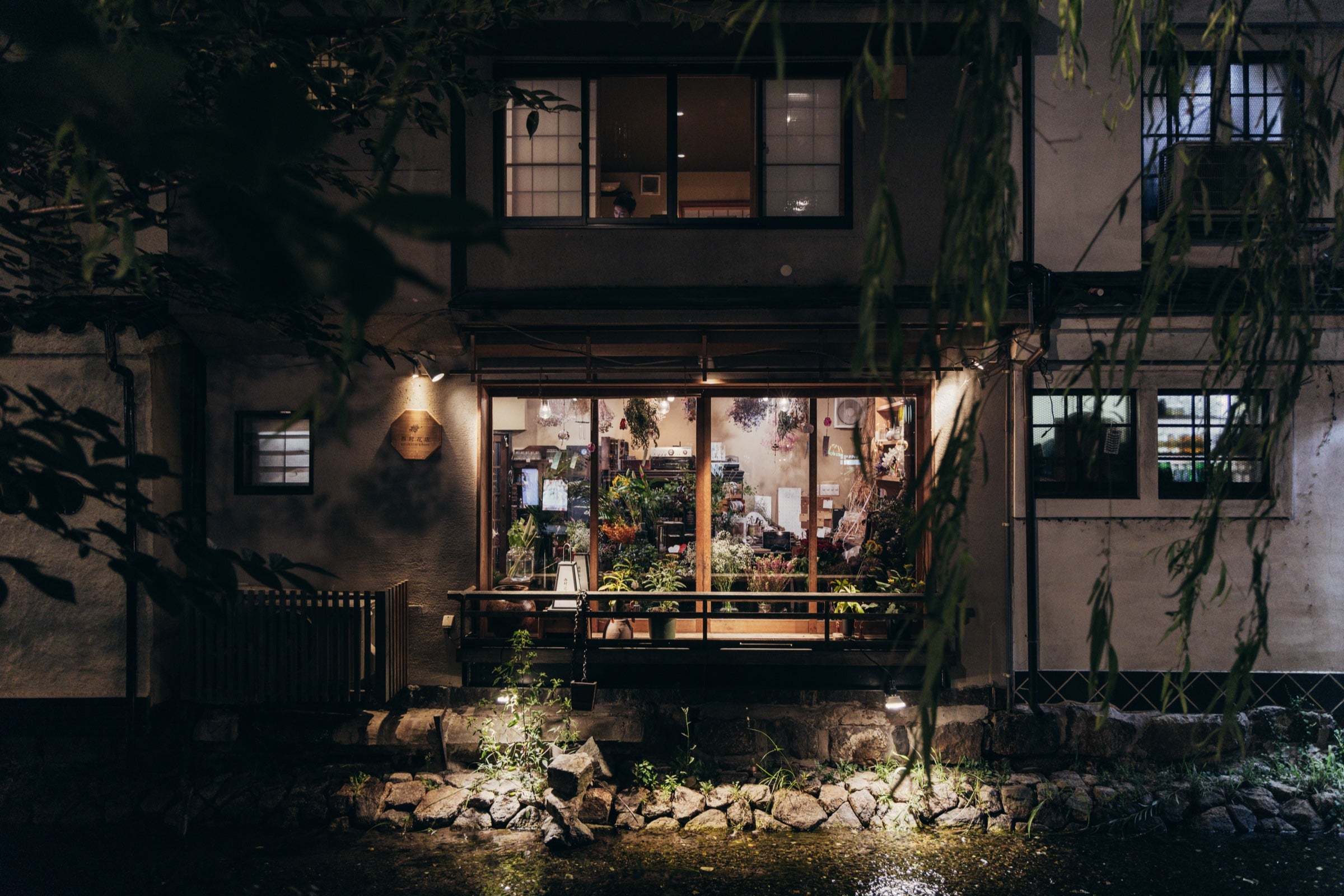 Maison traditionnelle japonaise éclairée au bord d'un canal derrière des branches de saule