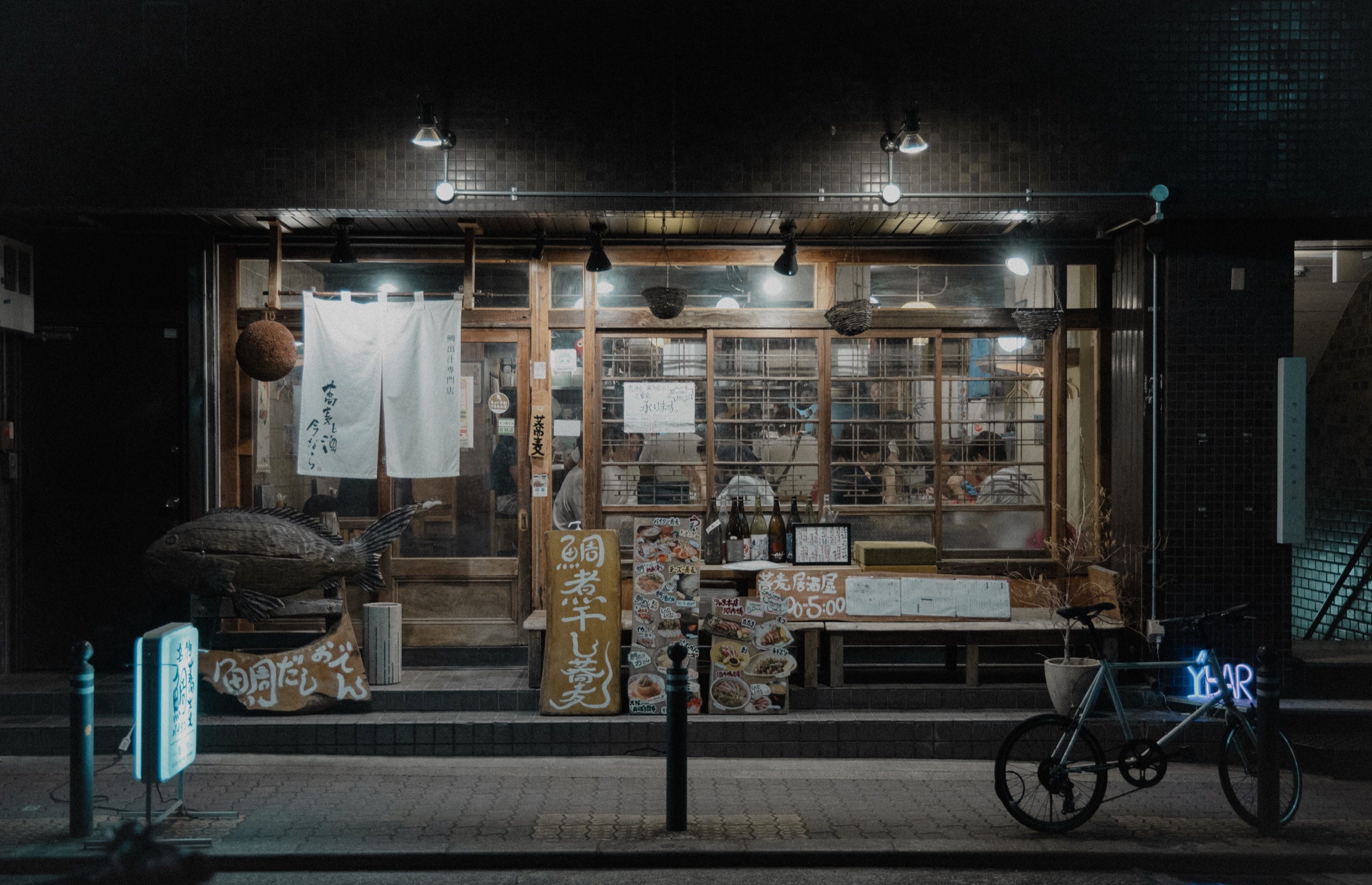 Devanture d'un izakaya la nuit avec un noren blanc et un vélo garé devant
