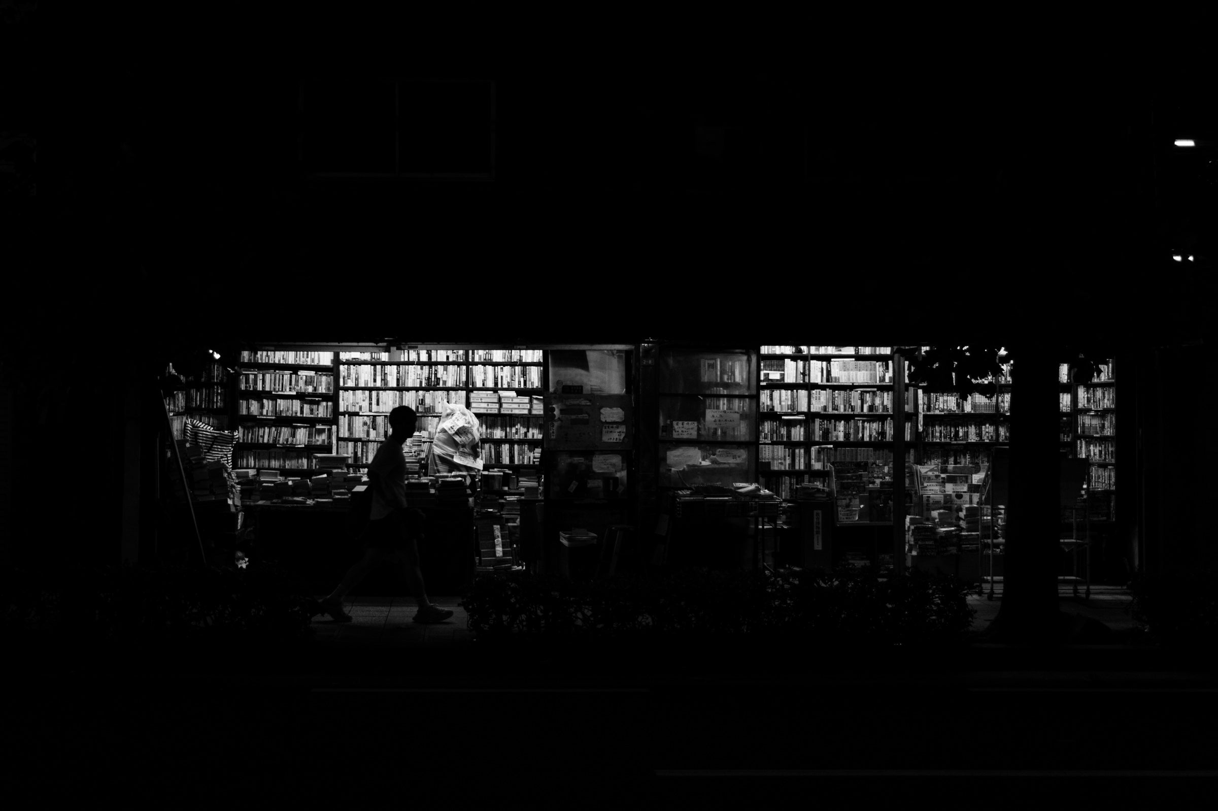 Silhouette d'un passant devant la vitrine éclairée d'une librairie de nuit