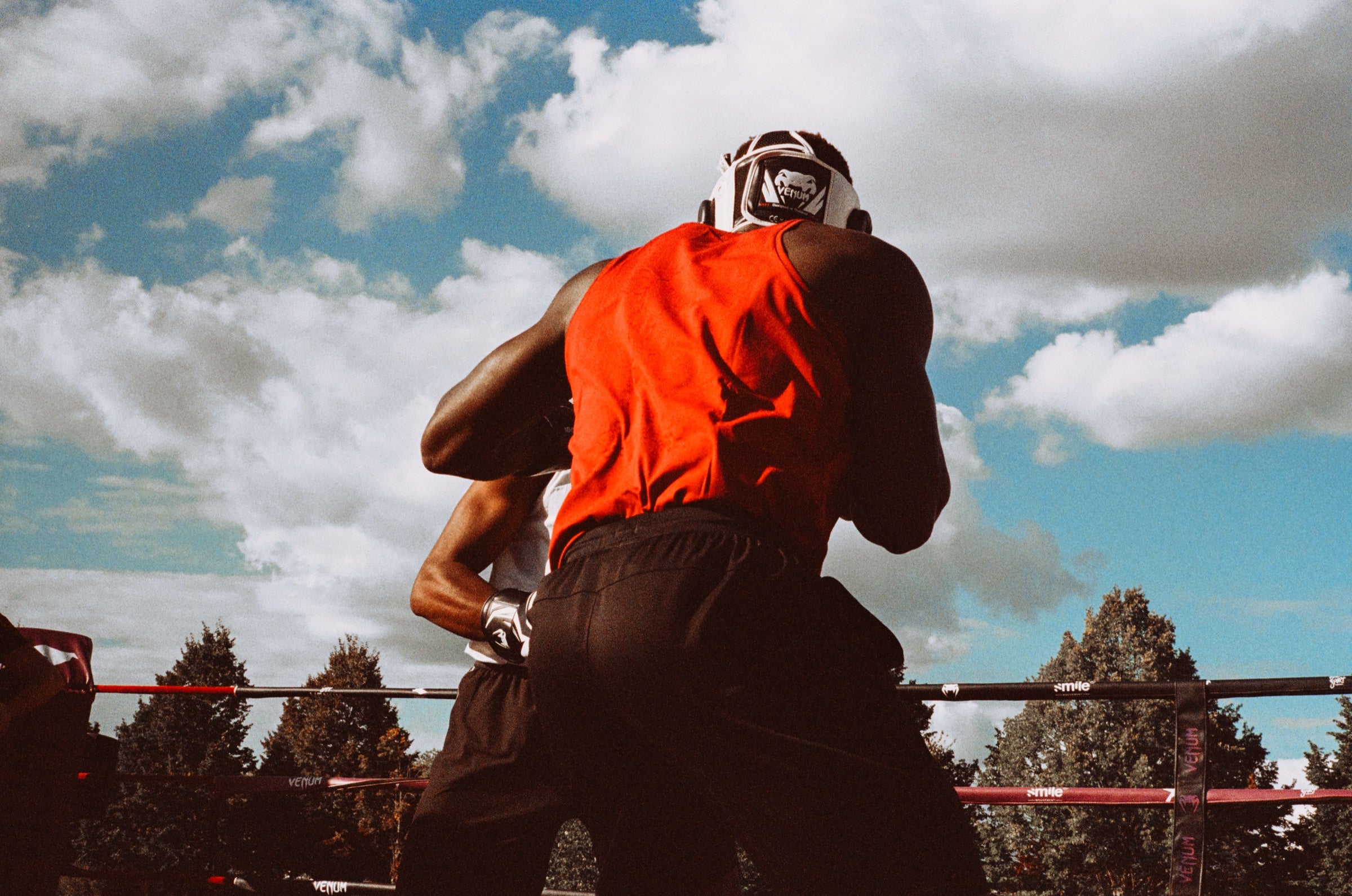 Boxeur de dos en débardeur rouge et casque de protection sur un ring en plein air